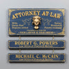 A rustic three-tier wooden sign set featuring a large top plaque and two smaller bottom plaques for a law office. The plaques are dark blue with gold lettering and ornate gold borders, with a small gold blindfolded bust in the center of the top plaque.