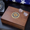 Wooden box with U.S. Navy emblem and sunglasses on a dark surface with an American flag in the background.
