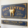 A decorative navy blue and gold dental sign on a wall, featuring the words 'PAINLESS DENTISTRY,' a large gold tooth sculpture in the center, and a smaller matching nameplate below reading 'SUSAN A. FRANK, DDS.
